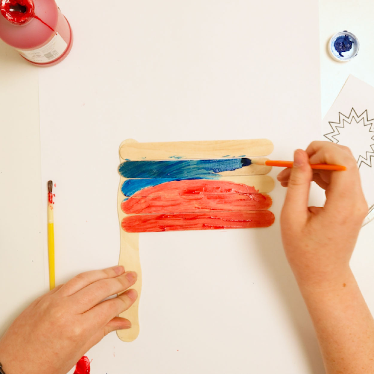 Paint the top half of a popsicle stick flag blue and the bottom half red to make a Juneteenth flag craft