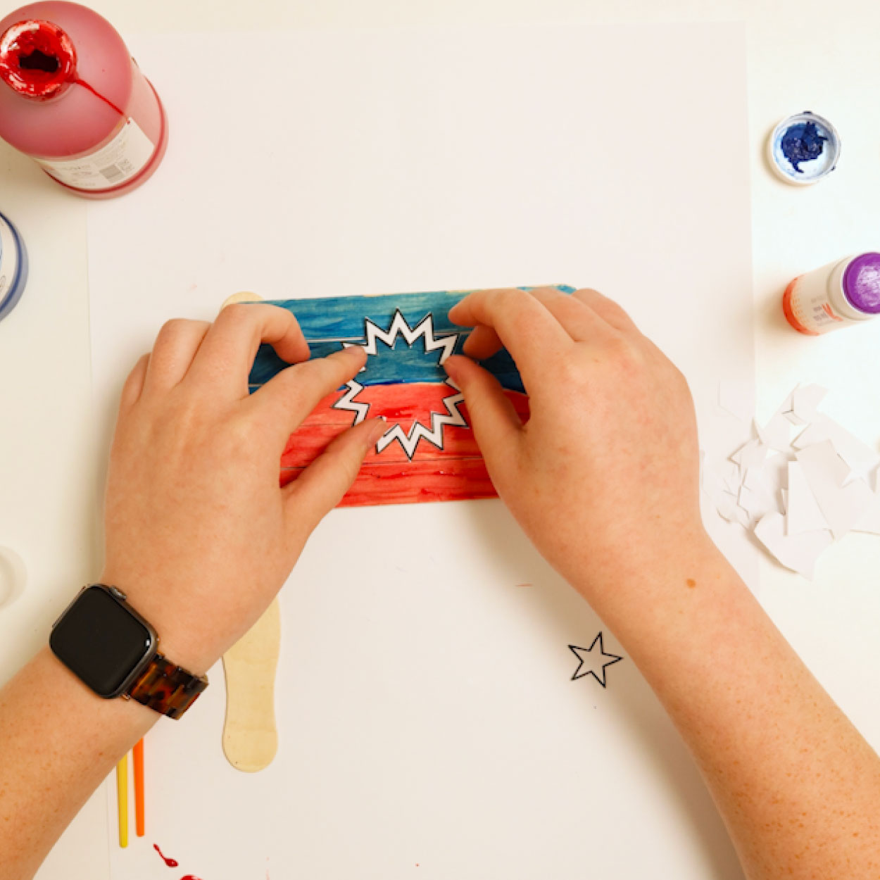 Glue a white paper bursting star cutout to the center of a painted popsicle stick Juneteenth flag